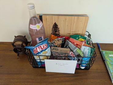 Welcome basket with snacks, pink lemonade, and a note on a wooden table.