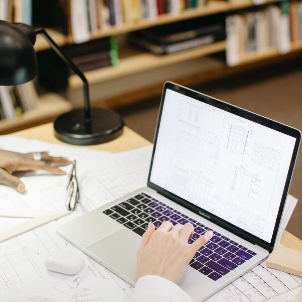 Persona trabajando con planos y computadora portátil en un escritorio.