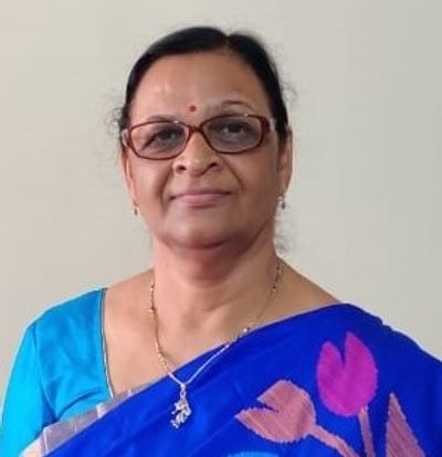 Woman in blue saree with glasses and a gentle smile.