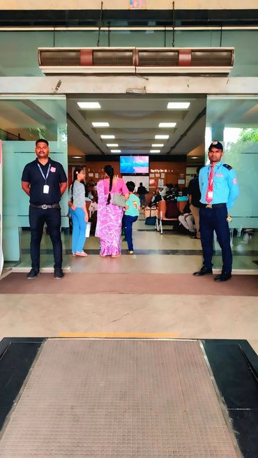 Security guards stand at the entrance of a busy waiting area with seated people inside.