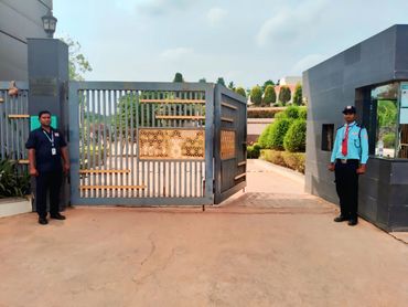 Two security guards stand at an open gate of a gated area.