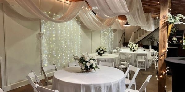 Elegant decorated event space with white drapes and floral centerpieces.