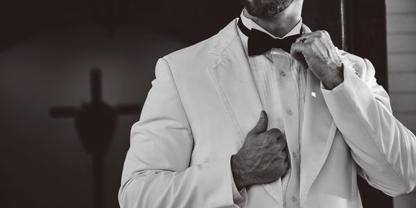 Man in white tuxedo adjusting bow tie.