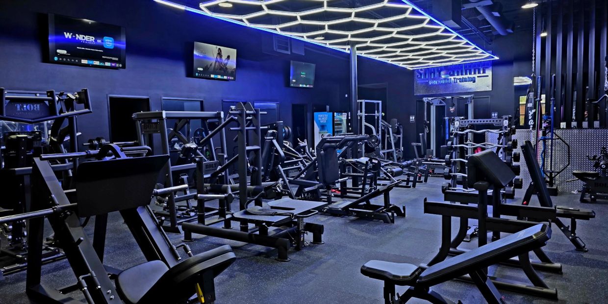 Modern gym with black workout machines and neon ceiling lights.