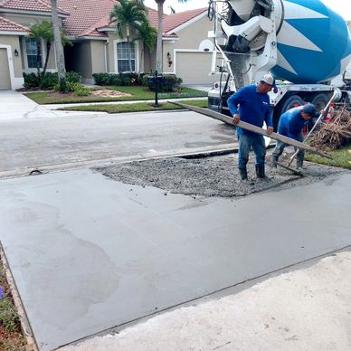 Workers pouring and smoothing concrete on a residential driveway.
