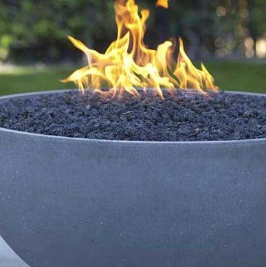 Modern fire pit with flames over black lava rocks in a garden.