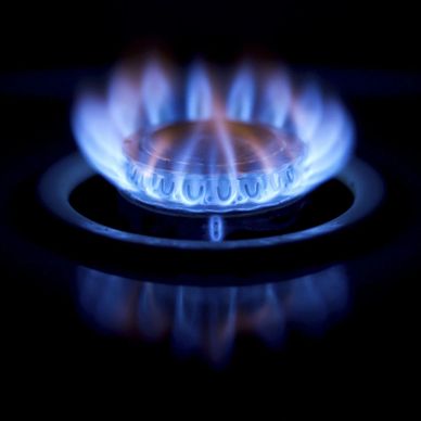 Blue flames burning on a gas stove burner in a dark setting.
