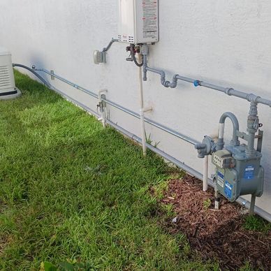 Gas meter and pipes attached to a house exterior wall with green grass.
