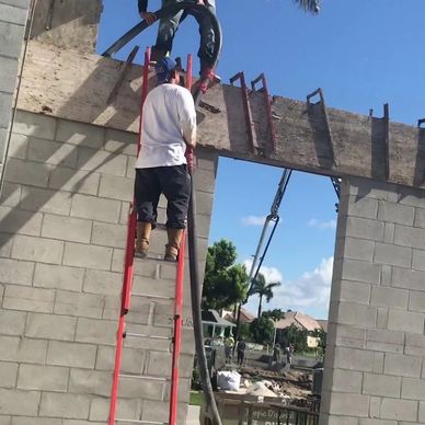 Construction workers on ladders building a concrete block structure under clear skies.