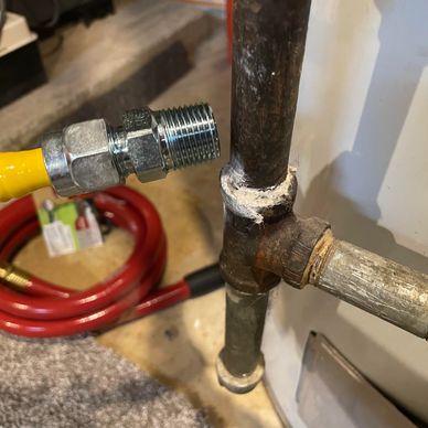 Hand holding a yellow gas hose fitting near a rusty pipe connection.