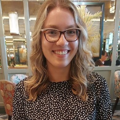 Smiling woman with glasses in a patterned blouse sitting in a cozy restaurant.