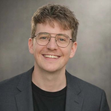 Smiling young man with glasses in a blazer.