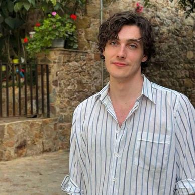 Young man with curly hair in a striped shirt outdoors.