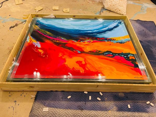 Abstract resin painting with vibrant red, orange, and blue hues in a wooden frame.