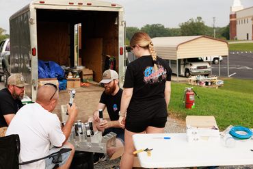 Group preparing fireworks next to an open trailer and table outdoors.