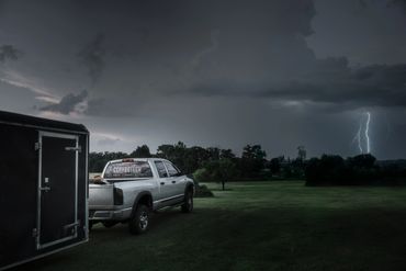 Truck with trailer parked on grass during a lightning storm at dusk.