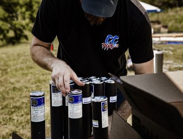 Person handling fireworks tubes outdoors, wearing a CC Pyro shirt.