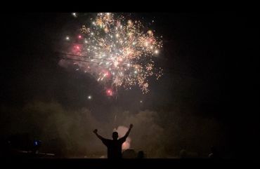 Silhouette of a person celebrating under vibrant fireworks at night.