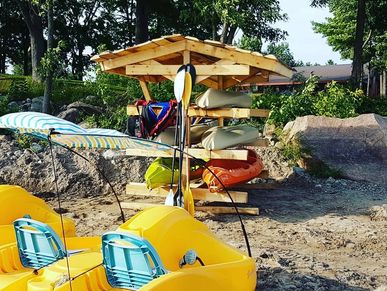 Yellow pedal boats and kayaks stored on a sandy shore near trees.