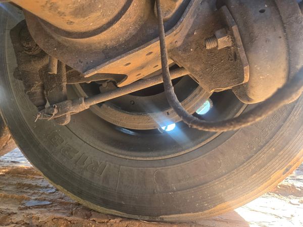 Underside view of a dusty vehicle tire and suspension components.