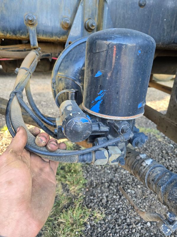 Hand holding a hose connected to a mechanical part with worn black paint.