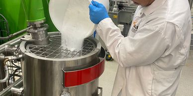 A person in gloves pours powder into a stainless steel machine.