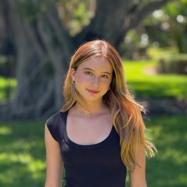 Young woman with long hair posing outdoors in sunlight.