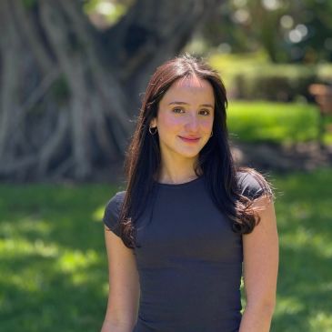 Young woman smiling outdoors with sunlight and greenery.