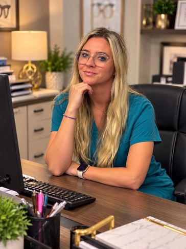 Young woman in scrubs at her desk in an office.