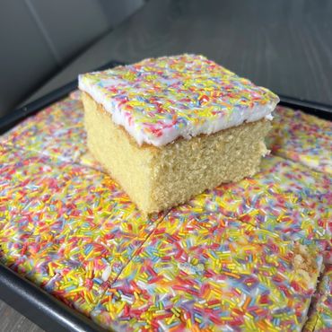 Square vanilla cake with white frosting and colorful sprinkles.