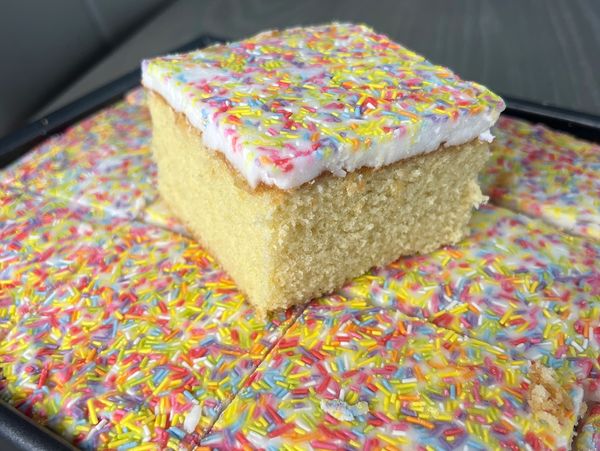 Square vanilla cake with white frosting and colorful sprinkles.