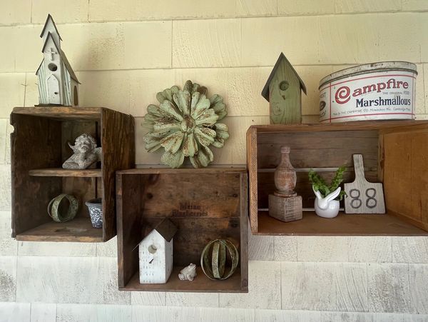 Rustic wooden shelves with birdhouses, decorative items, and a vintage marshmallow tin.