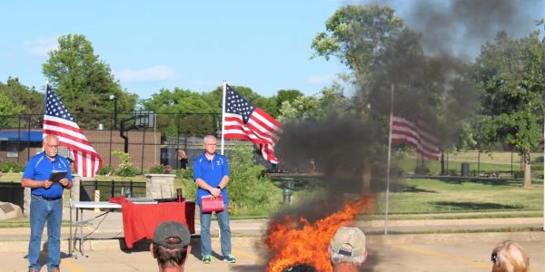 People stand near burning object with American flags in background.