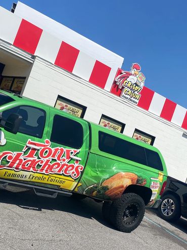 A green Tony Chachere's truck parked outside a Crispy Cajun Fried Chicken restaurant.