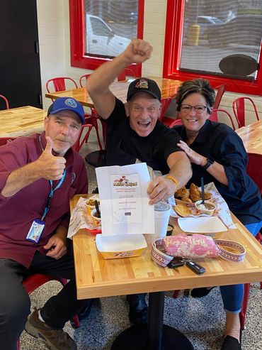 Three cheerful people at a restaurant table celebrating with food and a gift card.