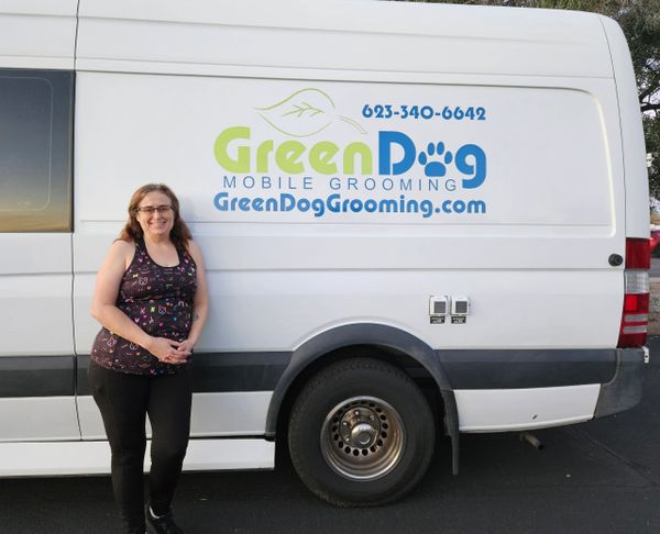 Woman standing beside GreenDog Mobile Grooming van with business details.