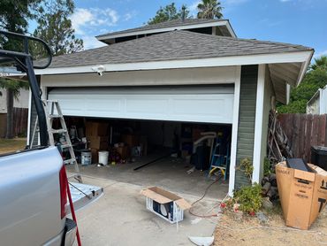Partially opened garage door with clutter and a ladder inside a residential garage.