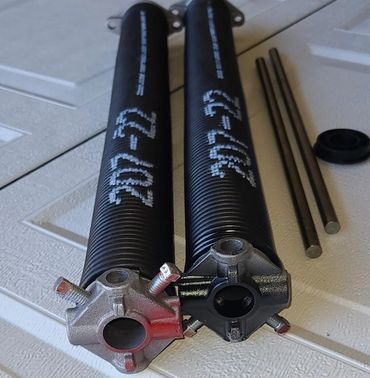 Two black garage door torsion springs with mounting hardware on a textured surface.