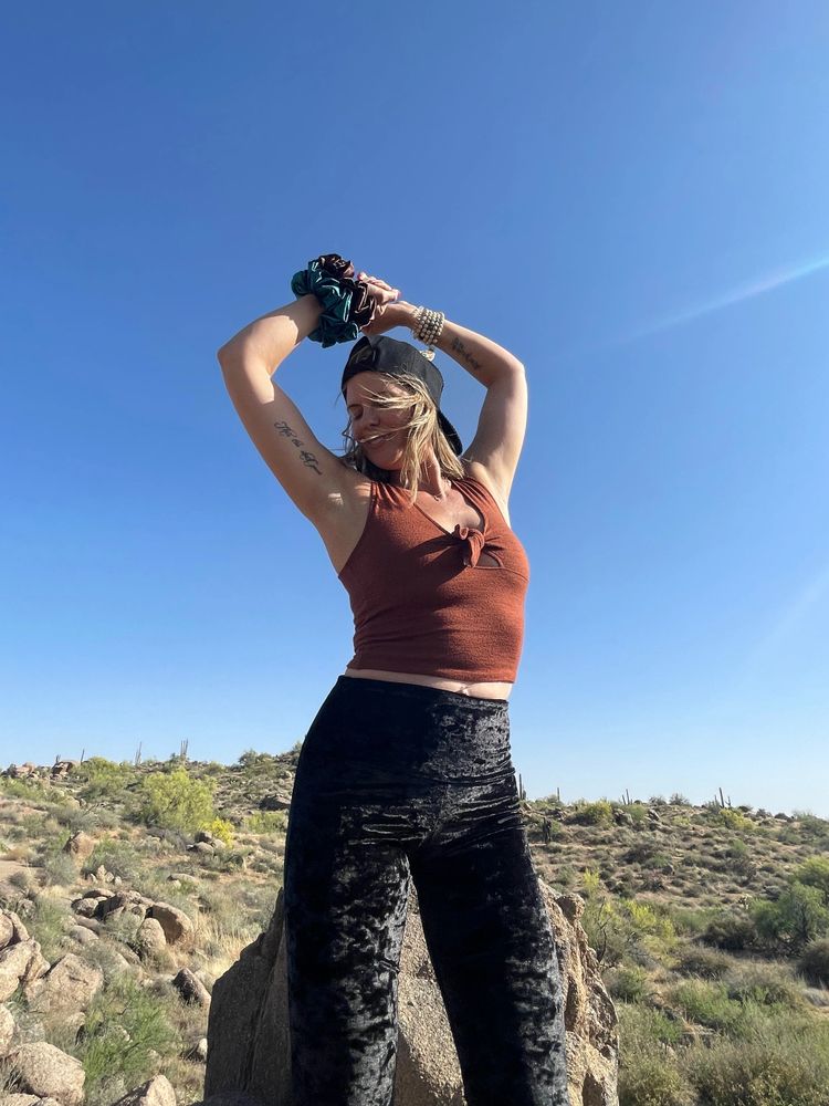 Woman poses joyfully outdoors against a clear blue sky.