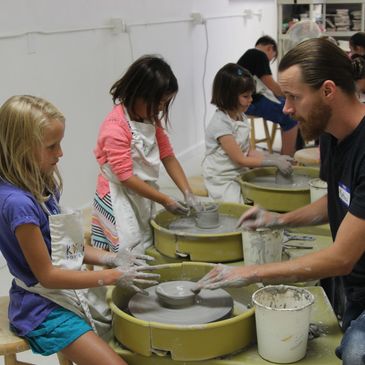 Children learning pottery with an instructor in a ceramics class.
