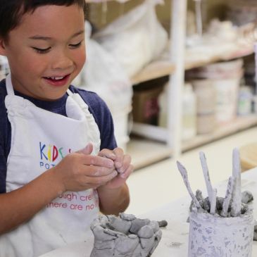 Child happily sculpting with clay at a pottery workshop.