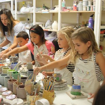 Children painting pottery in an art class with guidance from an instructor.