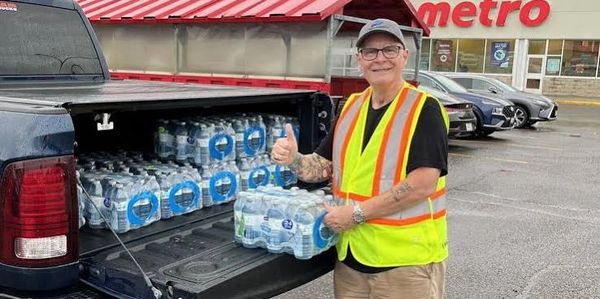 Man with safety vest shows thumbs up by water bottles in truck.