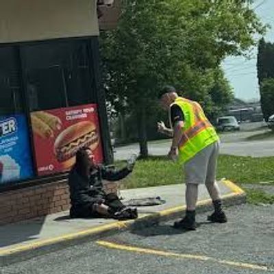 A man in a safety vest helping a person sitting on the curb.