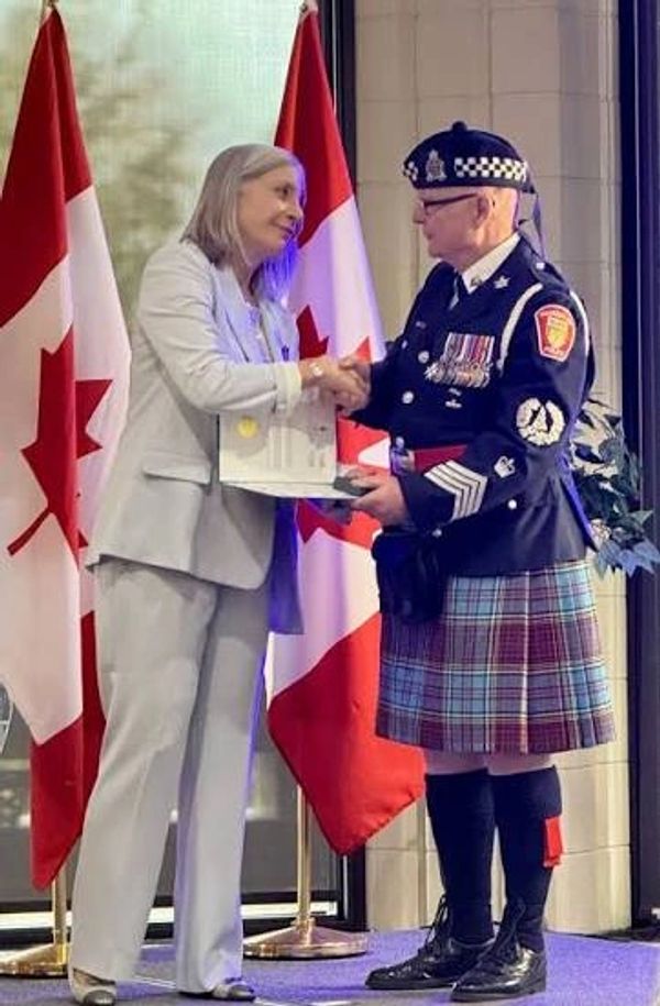 Woman presenting award to man in uniform and kilt.