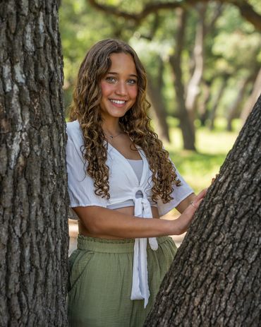 Liberty Hill girl smiling, standing between tree limbs