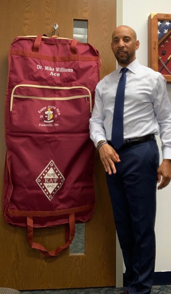 A man wearing a tie posing beside red mike bag