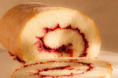 A sliced jelly roll cake with a light sponge and red jam swirl.