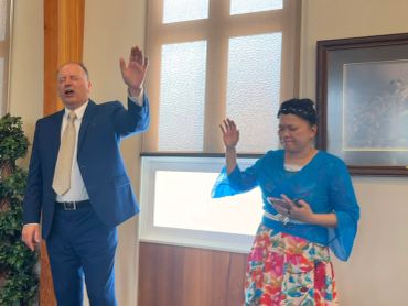 Two individuals raising their hands in a formal setting, possibly during a prayer or speech.