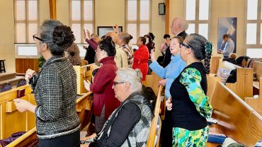 People engaged in worship inside a church with wooden pews.